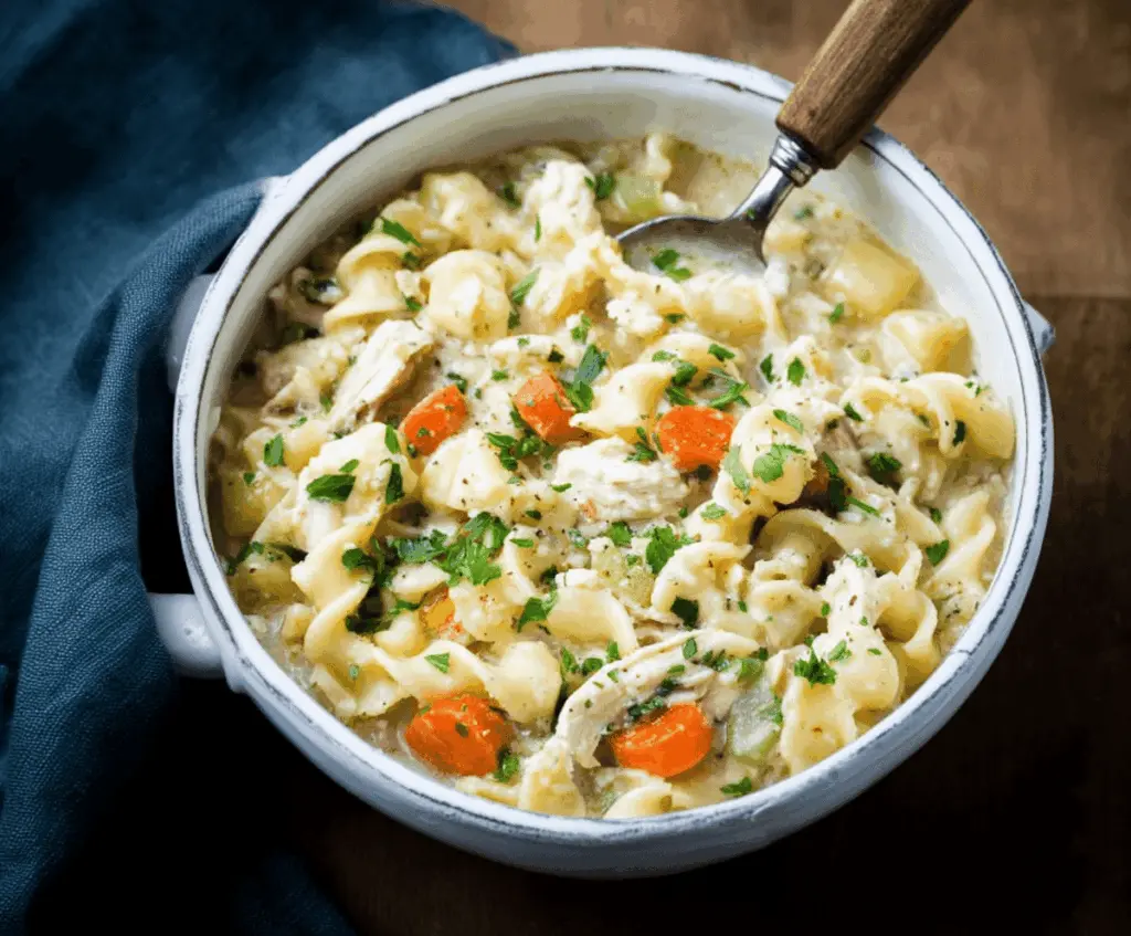 A bowl of warm Parmesan Chicken Noodle Soup garnished with fresh herbs and grated Parmesan cheese, featuring tender chicken, noodles, and vegetables in a flavorful broth.