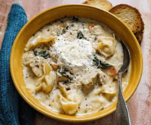 A bowl of creamy white lasagna soup topped with melted cheese, fresh basil, and crispy garlic bread on the side, showcasing a comforting Italian-inspired dish