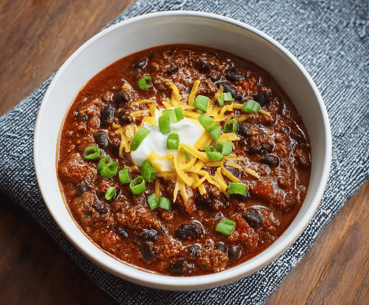 A bowl of hearty black bean chili topped with fresh cilantro and diced onions, served with tortilla chips on the side.