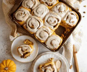 Pumpkin Cinnamon Rolls topped with Maple Frosting and served with a cup of coffee, perfect for fall mornings
