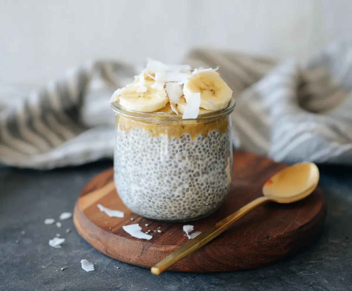 Delicious Banana Coconut Milk Chia Seed Pudding in a glass bowl with fresh banana slices and shredded coconut on top.