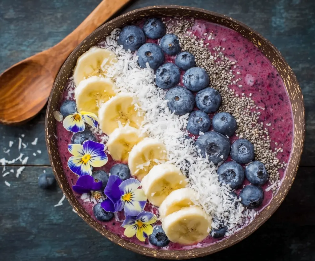 Healthy blueberry smoothie bowl topped with fresh berries and granola on a wooden table.