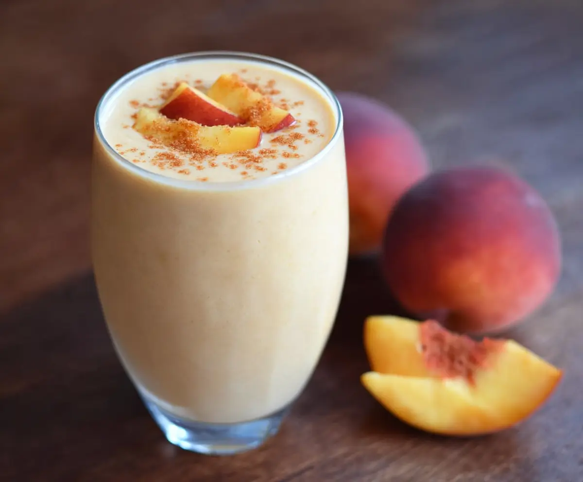 Refreshing peach protein smoothie in a glass with fresh peach slices and a straw, perfect for a healthy breakfast.
