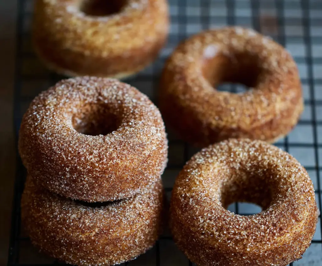 Delicious sourdough apple cider donuts coated with cinnamon and sugar on a rustic serving plate.