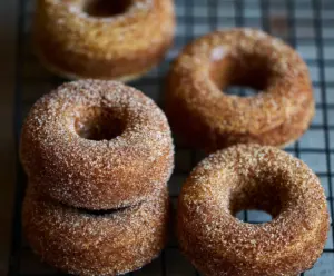 Delicious sourdough apple cider donuts coated with cinnamon and sugar on a rustic serving plate.