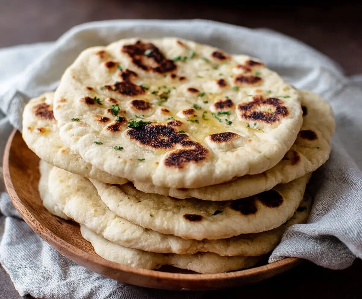 Homemade sourdough discard naan bread, soft and fluffy with golden crust, on a rustic wooden surface.