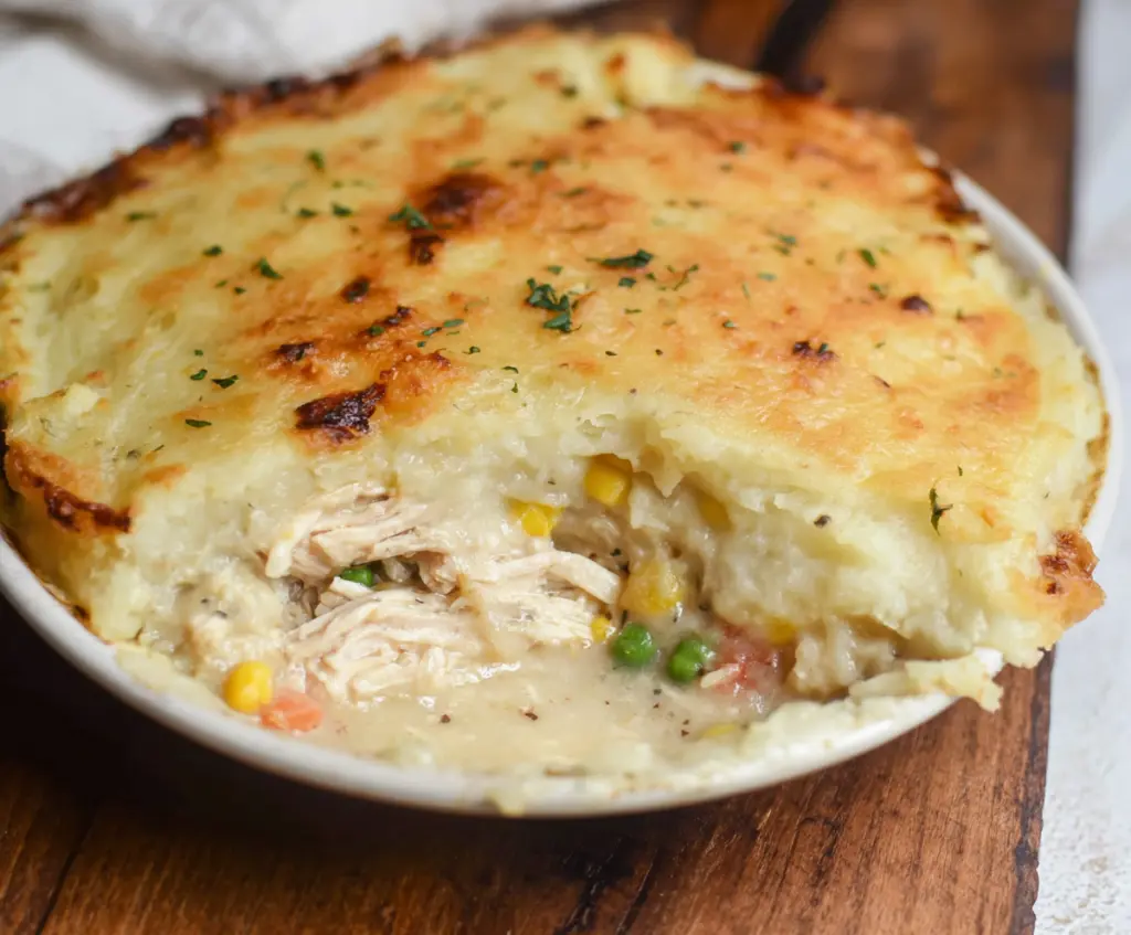 Delicious rotisserie chicken shepherd's pie served in a rustic dish with mashed potatoes and peas.