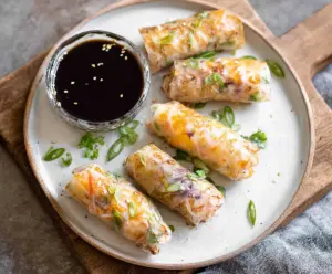 Crispy Air Fryer Rice Paper Rolls filled with fresh vegetables and herbs on a white plate.