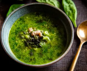 Vibrant green soup with pesto, fresh greens, and beans in a bowl, highlighting a healthy, vegetarian dish.
