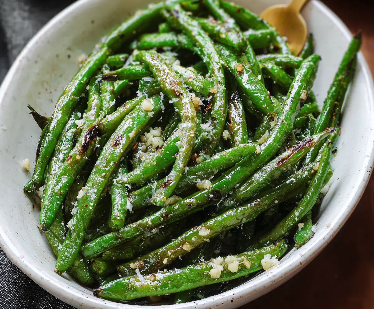 Delicious roasted green beans seasoned with garlic and herbs on a white plate.